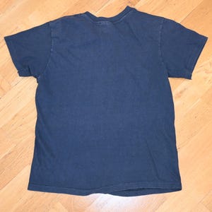May include: A navy blue short-sleeved t-shirt. The shirt is made of a soft material and has a crew neck. The shirt is laid flat on a wooden surface.