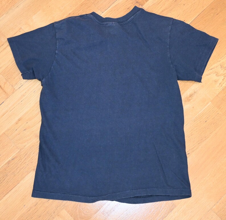 May include: A navy blue short-sleeved t-shirt. The shirt is made of a soft material and has a crew neck. The shirt is laid flat on a wooden surface.