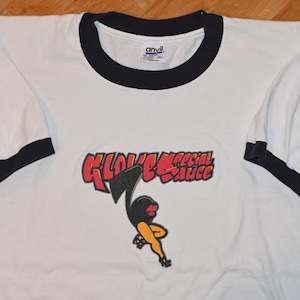 May include: White ringer t-shirt with black trim on the collar and sleeves. The shirt features a graphic of a running cartoon figure with the words "GLOVE Special Sauce" in red and black.