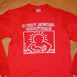 Könnte beinhalten: Rotes Langarm-T-Shirt mit einer weißen Grafik eines Strichmännchens, das ein anderes Strichmännchen hält. Die Grafik befindet sich in einem Kasten mit dem Text "A Very Special Christmas" darüber.
