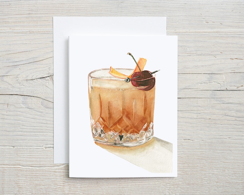 This card features a watercolor painting of an Old Fashioned cocktail in a faceted glass, garnished with an orange peel twist and a cherry on a cocktail pick. The drink casts a subtle shadow, and the background is simple white, adding elegance.