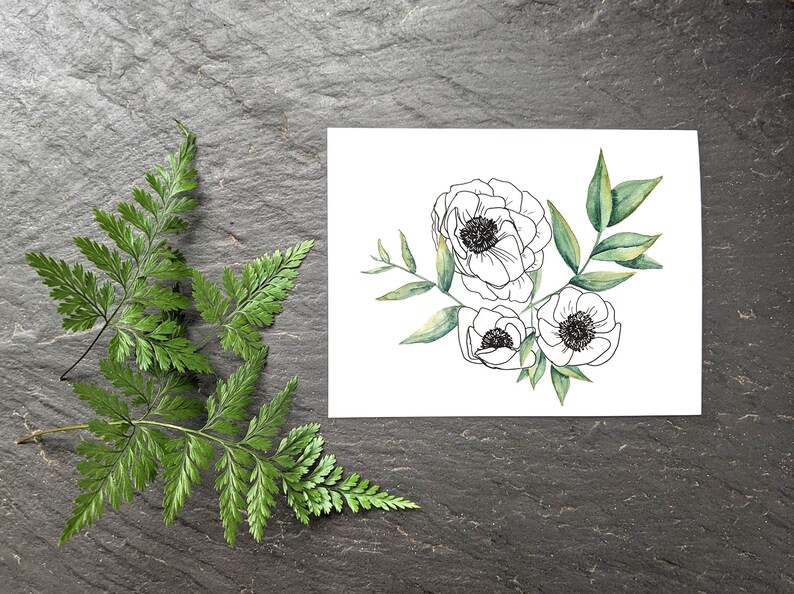 Pu&ograve; includere: Un biglietto bianco con un disegno in bianco e nero di tre fiori e foglie verdi. I fiori sono stilizzati e assomigliano ad anemoni. Il biglietto &egrave; su uno sfondo grigio scuro.
