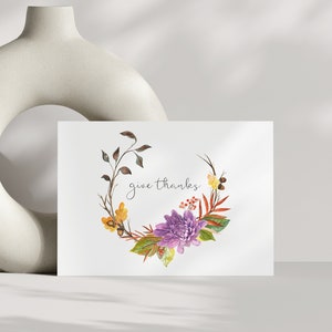 May include: A white card with a watercolor illustration of a floral wreath with purple flowers, yellow leaves, and brown branches. The text "give thanks" is written in cursive on the card.