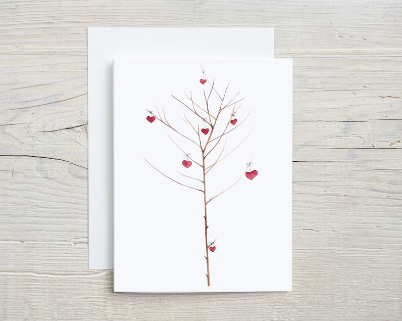This card displays a minimalist watercolor illustration of a bare, slender tree with delicate branches. Small red heart ornaments hang from various branches, tied with a thin string. The simple background accentuates the tree's elegance and warmth.