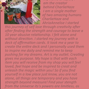 May include: A woman in a red dress stands in front of a table with a sign that reads "Charlie Haze". The text on the sign is a quote about self-love and creativity. The woman is smiling and holding a bouquet of flowers.