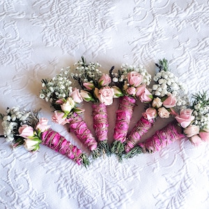 Puede incluir: Siete ramos de flores rosas y blancas envueltos en cordel rosa y marrón. Los ramos están atados con cordel y tienen pequeñas flores blancas y rosas rosas.