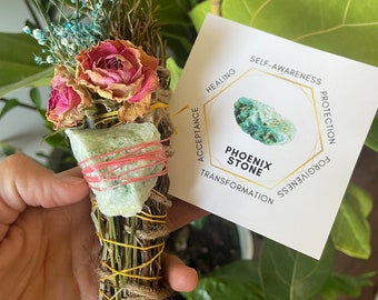 May include: A green crystal smudge stick with dried flowers and a tag that reads "Phoenix Stone" and lists the stone's properties: self-awareness, protection, forgiveness, healing, acceptance, and transformation.