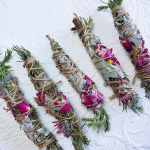 May include: Six bundles of dried herbs and flowers tied with twine. The bundles are made with rosemary, lavender, sage, and pink flowers.