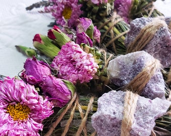 May include: A smudge stick with dried flowers and purple crystals wrapped in twine. The flowers are pink and purple and the crystals are amethyst.