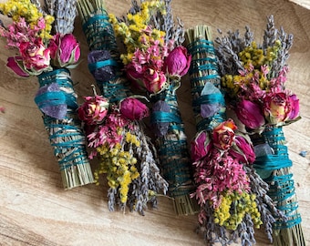 May include: Five bundles of dried herbs and flowers wrapped in teal thread, each featuring lavender, yellow goldenrod, and pink rosebuds. Each bundle is accented with a small, raw purple or clear crystal stone secured by the teal string.
