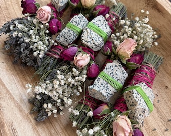 May include: A collection of bundles featuring dried lavender, white baby's breath, and pink rosebuds. Each bundle is tied with bright green or pink string and includes a small, speckled dalmatian jasper stone secured to the exterior of the stems.