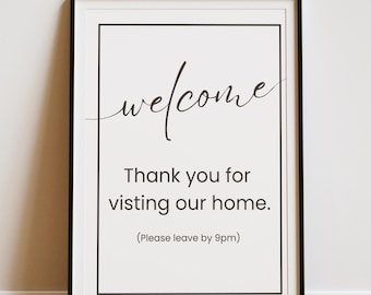 May include: A black framed print with white text that reads "welcome" in cursive, "Thank you for visiting our home." and "(Please leave by 9pm)".