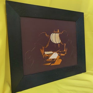 May include: A framed print of a vintage illustration depicting two women in traditional Japanese clothing sitting at a table with a lantern. The women are silhouetted against a dark background, and the lantern casts a warm glow on the scene.