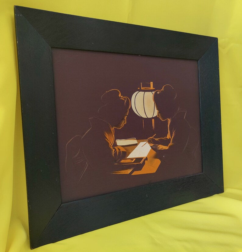 May include: A framed print of a vintage illustration depicting two women in traditional Japanese clothing sitting at a table with a lantern. The women are silhouetted against a dark background, and the lantern casts a warm glow on the scene.