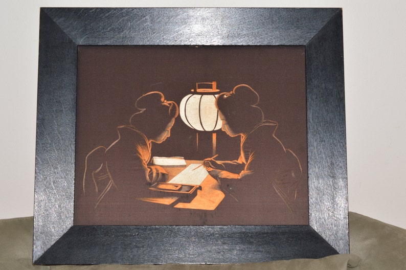 May include: A framed artwork depicting two figures in traditional Japanese clothing, seated at a table with a lit paper lantern. The figures are silhouetted against a dark background, creating a sense of mystery and intimacy.