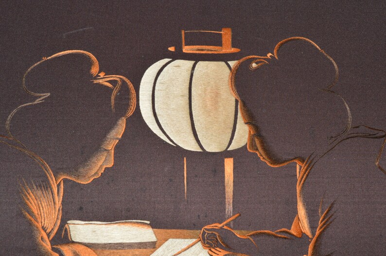 May include: Two women in traditional Japanese clothing are seated at a table under a paper lantern. One woman is writing in a book while the other looks on.