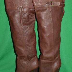 May include: A pair of brown leather knee-high boots with a block heel and buckle detail.