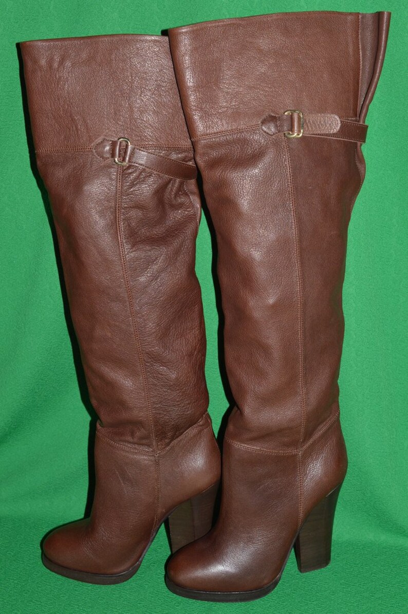 May include: A pair of brown leather knee-high boots with a block heel and buckle detail.