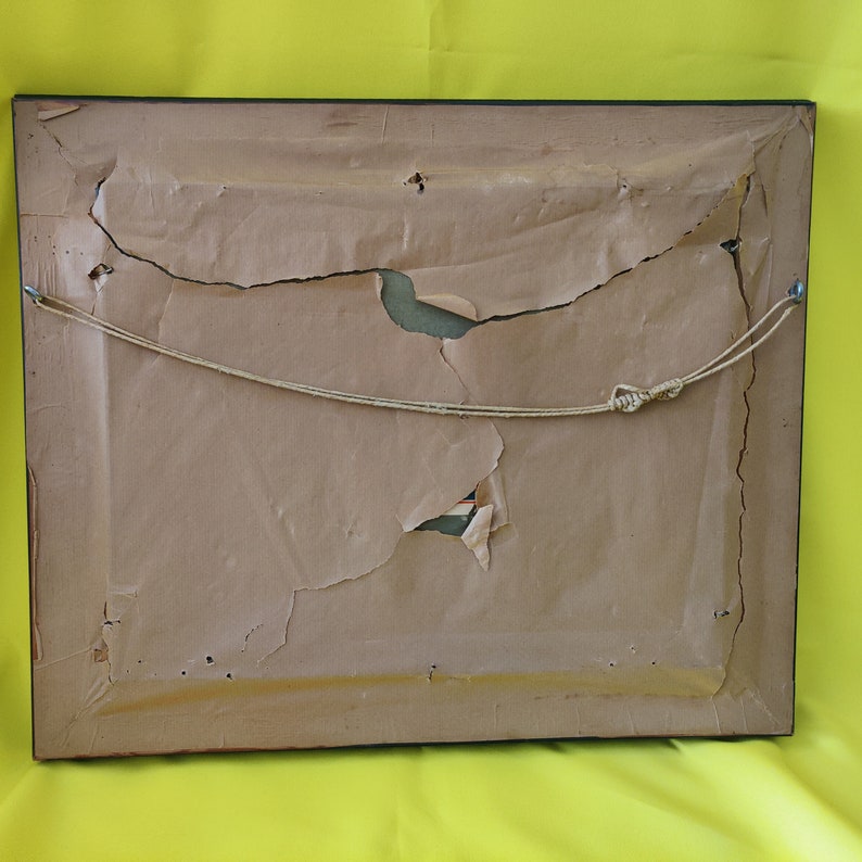 May include: The back of a framed picture with a brown paper backing. The paper is torn and ripped in several places. A string is attached to the frame for hanging.
