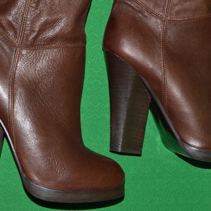 May include: A pair of brown leather knee-high boots with a chunky heel. The boots have a pointed toe and a zipper on the back.