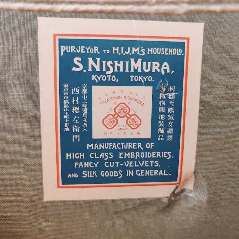 May include: A vintage label with blue and red borders, advertising S. Nishimura, a purveyor to the Imperial Household of Japan. The label states that the company is a manufacturer of high-class embroideries, fancy cut velvets, and silk goods in general. The label also includes the company's address in Kyoto and Tokyo.