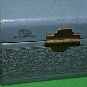 Pu&ograve; includere: Una scatola per gioielli blu chiaro con un design floreale in rilievo. La scatola ha una cerniera in ottone e un'etichetta che recita "Smilee Crafted Chicago Made in U.S.A."