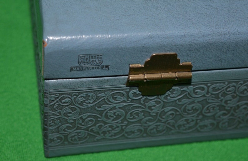 Pu&ograve; includere: Una scatola per gioielli blu chiaro con un design floreale in rilievo. La scatola ha una cerniera in ottone e un'etichetta che recita "Smilee Crafted Chicago Made in U.S.A."