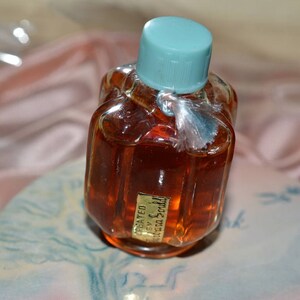 Pu&ograve; includere: Un piccolo flacone di vetro trasparente con un tappo blu chiaro e un liquido marrone all'interno. Il flacone ha un'etichetta con la scritta "Concentrated Extract of Scotch" in lettere dorate.