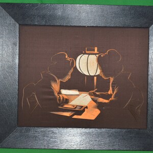 May include: A framed artwork depicting two figures in silhouette, seated at a table with a lamp. The figures are dressed in traditional Japanese clothing and appear to be writing or drawing. The artwork is set against a dark brown background.