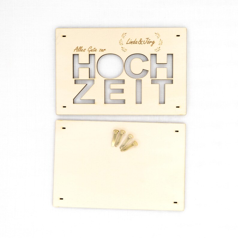 Pu&ograve; includere: Una targa rettangolare in legno chiaro con il testo tagliato al laser "Alles Gute zur HOCHZEIT" e "Linda & J&ouml;rg" con decorazioni a forma di foglia. &Egrave; incluso un secondo pannello rettangolare in legno semplice con quattro piccoli perni dorati.