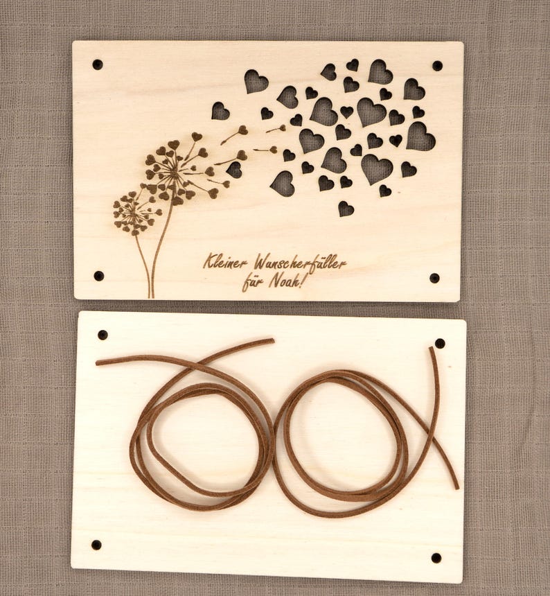 May include: A wooden card with a dandelion design and the text "Kleiner Wunscherf&uuml;ller f&uuml;r Noah!"  The card is accompanied by a brown cord.
