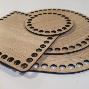 Könnte beinhalten: Drei hölzerne Strickringe in verschiedenen Größen. Die Ringe sind aus hellbraunem Holz mit einer Holzmaserung. Die Ringe haben Löcher an den Rändern zum Stricken.