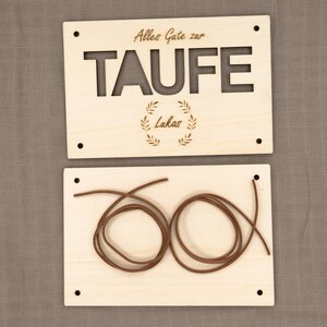 Puede incluir: Dos letreros de madera con el texto "Alles Gute zur Taufe Lakas" y un cord&oacute;n marr&oacute;n.
