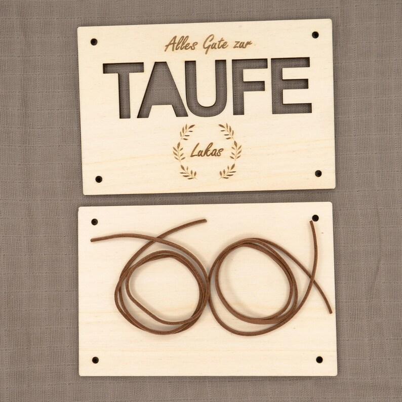 Puede incluir: Dos letreros de madera con el texto "Alles Gute zur Taufe Lakas" y un cord&oacute;n marr&oacute;n.