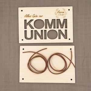 May include: Two wooden signs with the words "Alles Gute zur Kommunion" and "Aaron 27.04.2025" engraved on them. The signs are attached to a brown string.