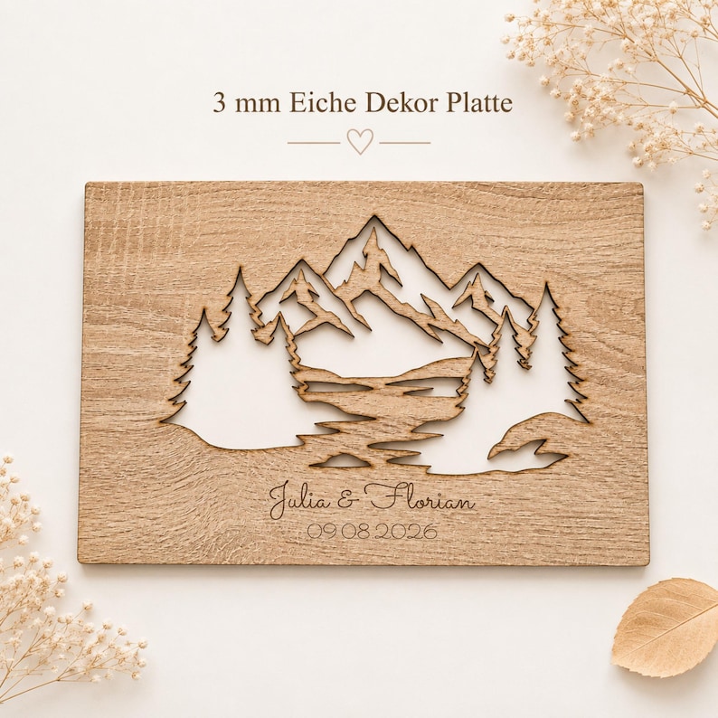 May include: A rectangular 3 mm oak decorative plaque featuring a laser-cut mountain and pine tree landscape. The wood surface displays natural grain patterns. Below the cutout, the text reads Julia & Florian and the date 09.08.2026.