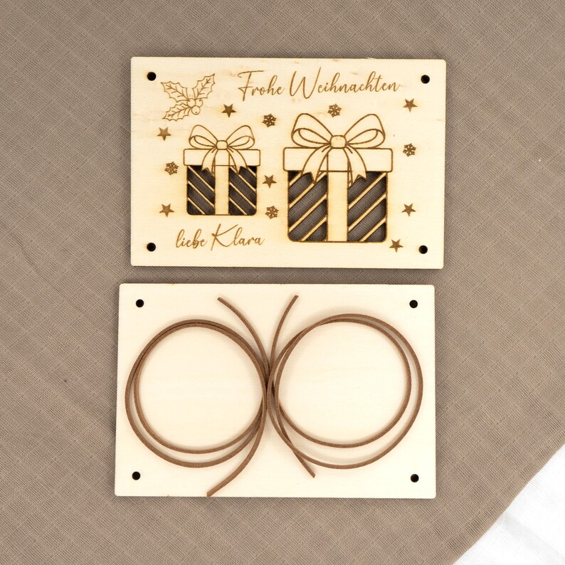 Pu&ograve; includere: Due ornamenti natalizi rettangolari in legno. L'ornamento superiore ha incise le parole "Frohe Weihnachten" e "liebe Klara", insieme a disegni di scatole regalo e stelle. L'ornamento inferiore ha due cordoncini marroni.