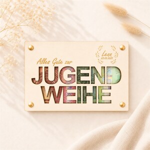 Könnte beinhalten: Eine rechteckige Holzplatte in hellem Farbton mit dem lasergeschnittenen Schriftzug "JUGENDWEIHE" und "Alles Gute zur" darüber. Die Buchstaben sind mit farbigen Geldscheinen hinterlegt. Sie enthält den Namen "Lenn", das Datum "03.05.2025" und vier goldfarbene Metallschrauben.
