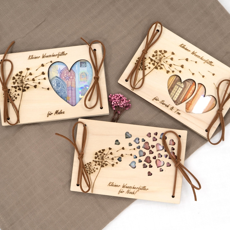 May include: Three wooden boxes with a dandelion design and a heart-shaped cutout. The boxes are tied with brown ribbon and have the text "Kleiner Wunscherf&uuml;ller" and a name on each box.