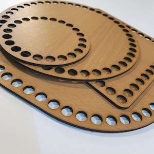 May include: Three wooden crochet hoops of different sizes, with a round, oval, and square shape. The hoops are made of light brown wood and have black holes around the edges.
