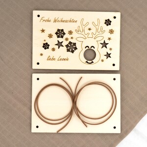 Pu&ograve; includere: Due decorazioni natalizie in legno. L'ornamento superiore presenta un disegno di renna con le parole "Frohe Weihnachten" e "liebe Leonie" incise nel legno. L'ornamento inferiore ha due corde marroni.