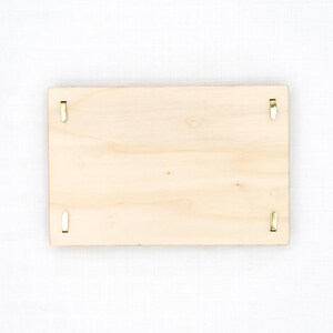 Pu&ograve; includere: Una targa rettangolare in legno di colore chiaro con una finitura a venature naturali e liscia. La targa presenta quattro piccole clip metalliche color oro posizionate vicino a ogni bordo, progettate per fissare oggetti sulla superficie.