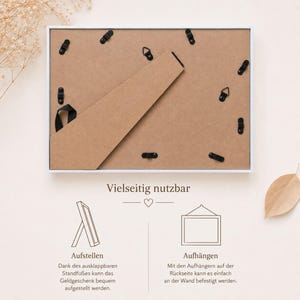 May include: A rectangular white picture frame shown from the back, featuring a brown backing board, a hinged support stand, and multiple black metal swivel clips. Below, text and line drawings illustrate two ways to display the frame: standing up or hanging on a wall.