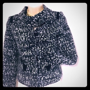 Puede incluir: Una chaqueta de tweed negra y blanca con un cierre de botón único. La chaqueta tiene cuello y mangas largas.