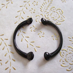 May include: A black metal bangle bracelet with rounded ends. The bracelet is on a white background with a gold floral pattern.