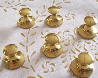 May include: Six gold-toned metal knobs with a round top and a round base. The knobs are arranged in a semi-circle on a white surface.
