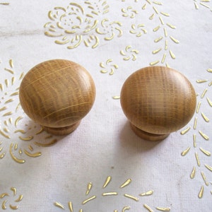 May include: Two wooden knobs with a light brown finish. The knobs are round and have a smooth surface.