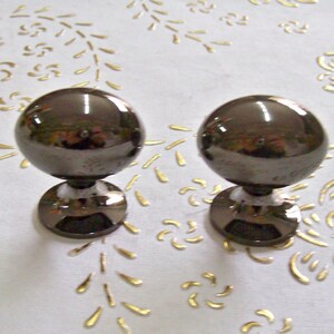 Op de afbeelding: Twee zwarte metalen kastknoppen met een ronde, glanzende, bolvormige bovenkant en een ronde basis.