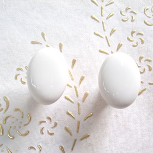 Könnte beinhalten: Zwei weiße Keramik-Schrankknöpfe mit einer glatten, abgerundeten Oberfläche.