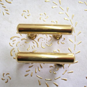 May include: Two gold-toned metal cabinet door pulls. The pulls are rectangular in shape and have a smooth, polished finish.